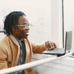 Programista z dredami pracuje z uśmiechem na laptopie w drodze