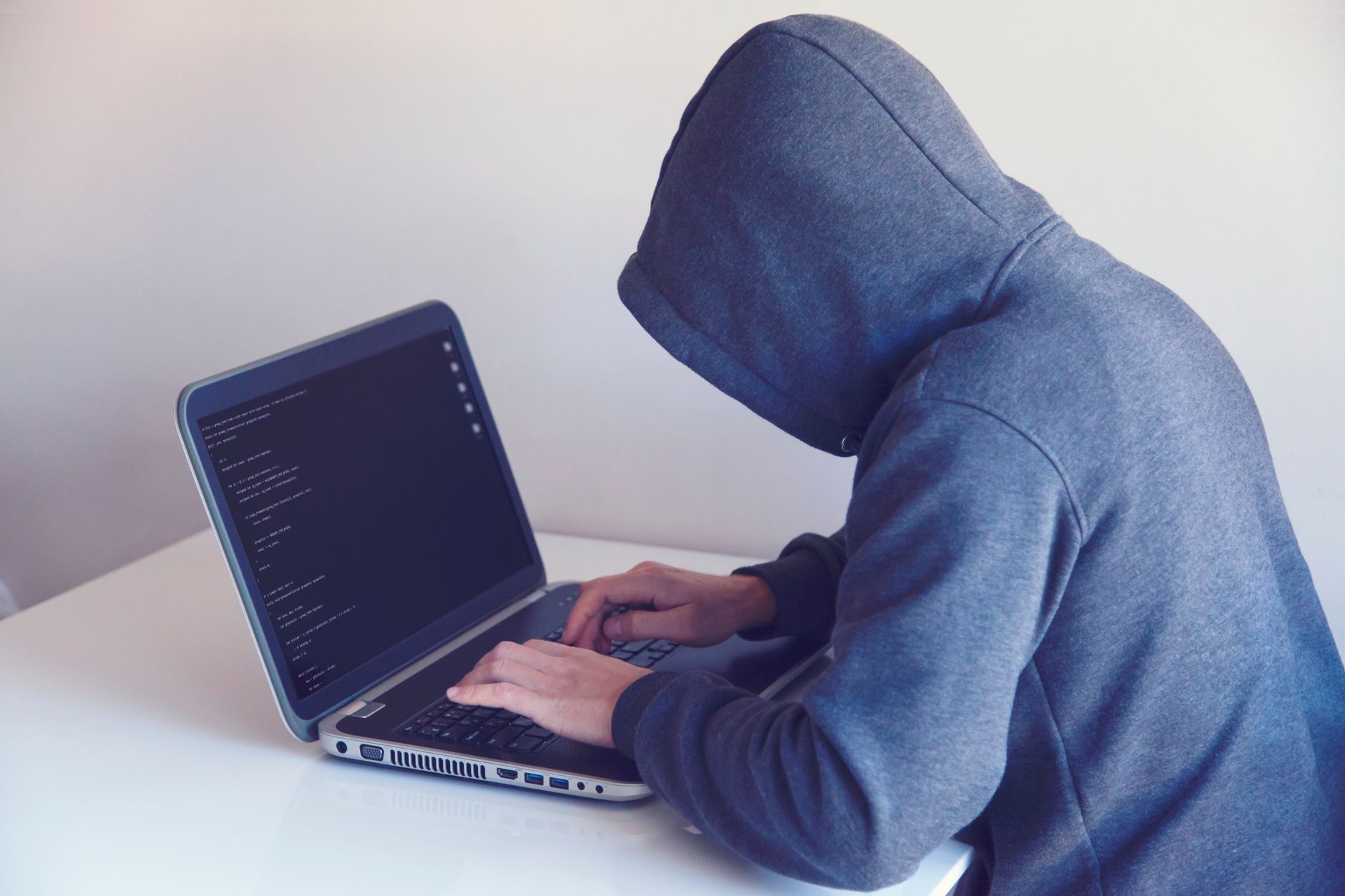 Haker w bluzie z kapturem pracuje przy laptopie w jasnym pomieszczeniu