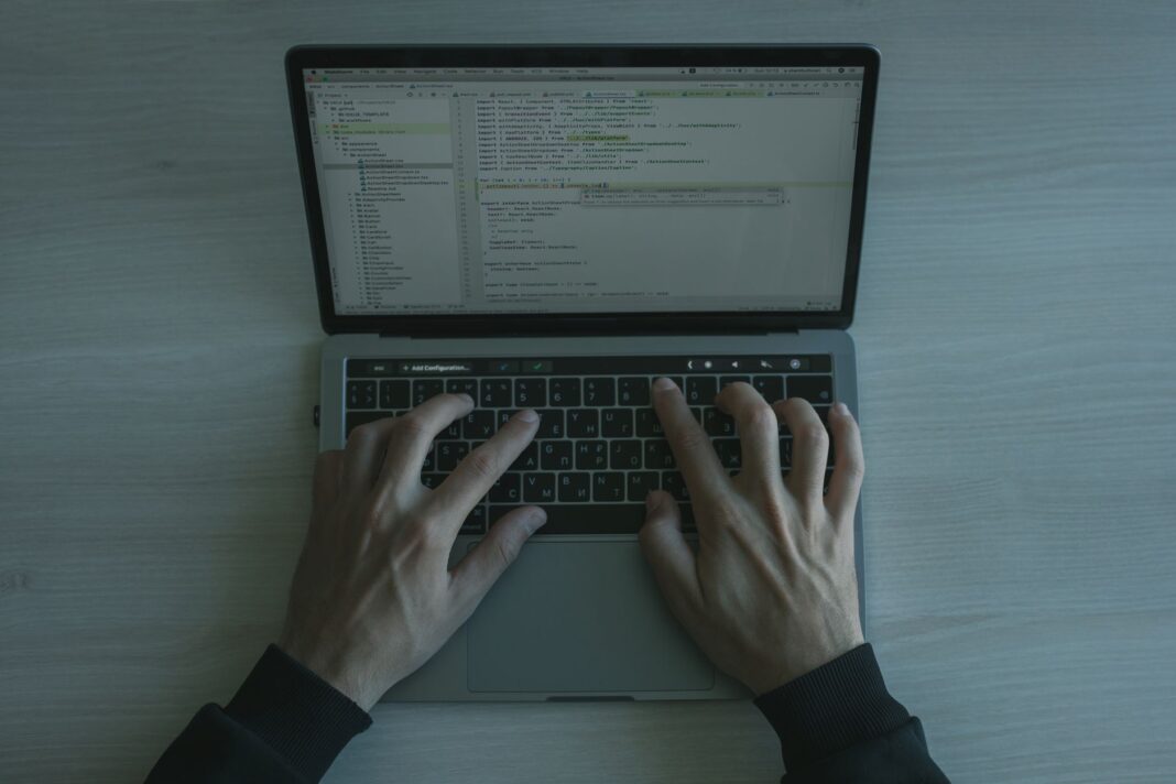 Programista przy laptopie piszący kod, zbliżenie na ekran i dłonie