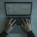 Programista przy laptopie piszący kod, zbliżenie na ekran i dłonie
