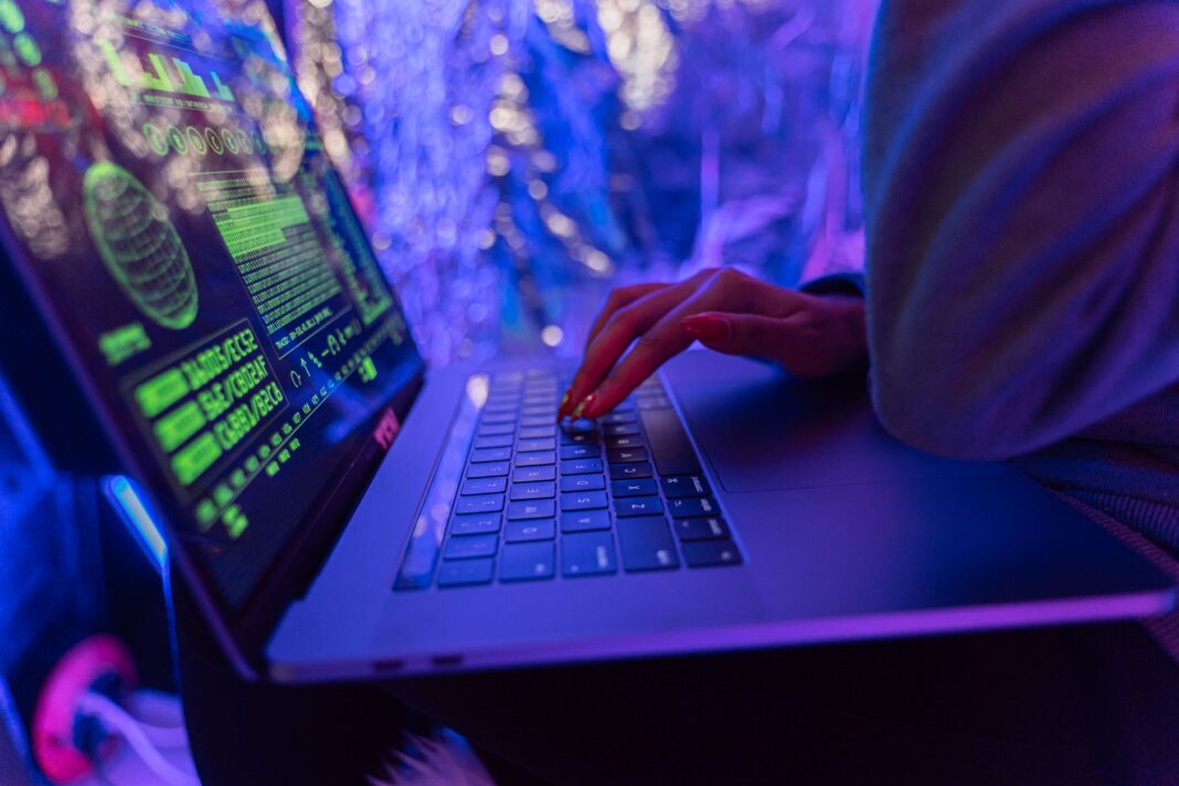 Ręce piszące na laptopie z grafiką cyberbezpieczeństwa w fioletowym świetle