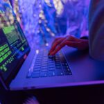 Zero-day w Twoich bibliotekach: jak monitorować zależności w projektach Ręce piszące na laptopie z grafiką cyberbezpieczeństwa w fioletowym świetle