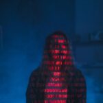 Zero Trust a VPN: jak połączyć stare tunelowanie z nowym podejściem do bezpieczeństwa sieci Sylwetka w cieniu z czerwonym kodem binarnym na twarzy na ciemnym tle