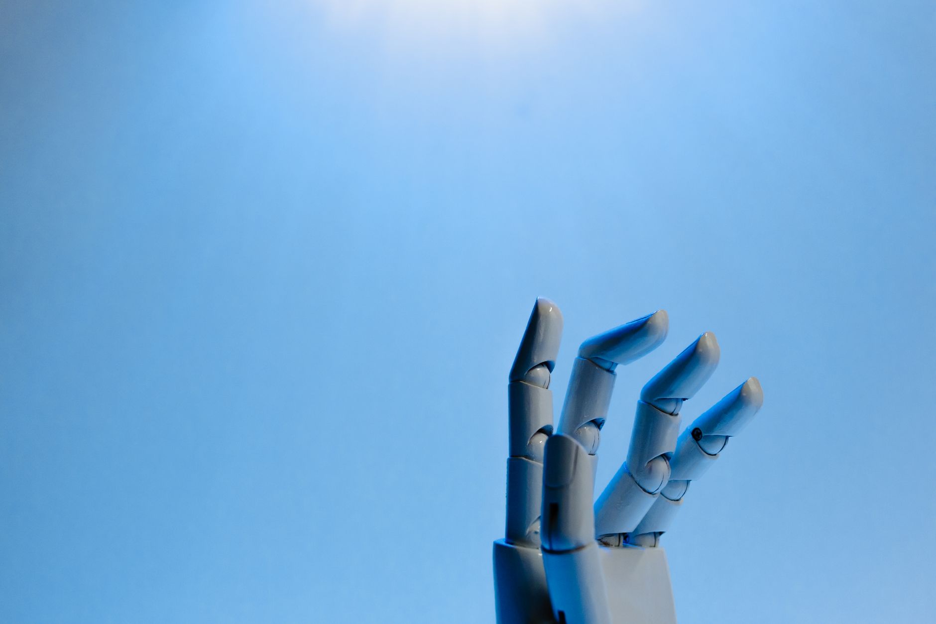 Metaliczna dłoń robota wyciągnięta w górę na niebieskim tle
